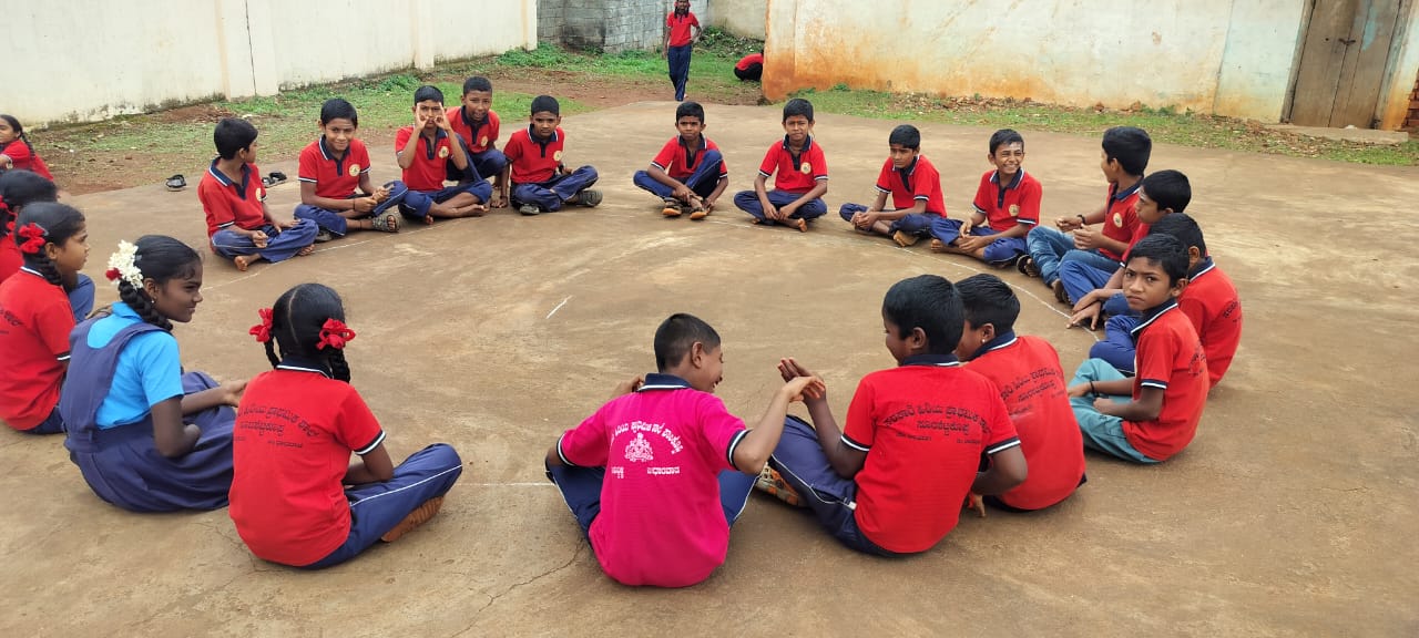 Students in red and blue uniforms sitting in circle for outdoor learning activity