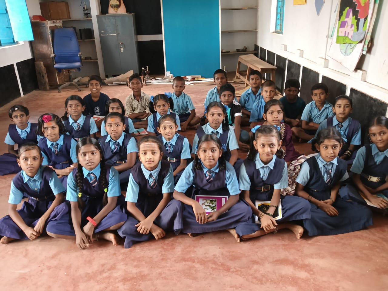 Female students in blue uniforms sitting attentively on classroom floor